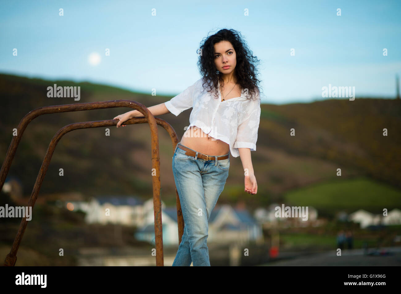 Una joven mujer morena delgada atractiva joven en la reflexión profunda, por ella misma, solo , lleva vaqueros y una camiseta blanca recortada blusa fuera al aire libre en las cálidas