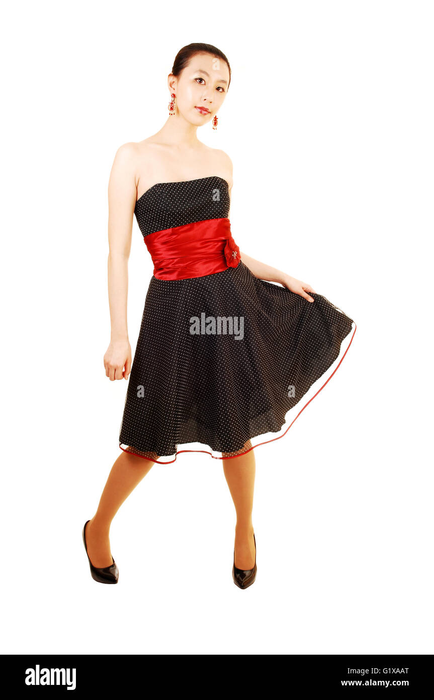 Una encantadora y tall joven mujer asiática en un vestido negro y rojo del cinturón para fondo blanco permanente, levantando su vestido en una SID Fotografía de stock Alamy