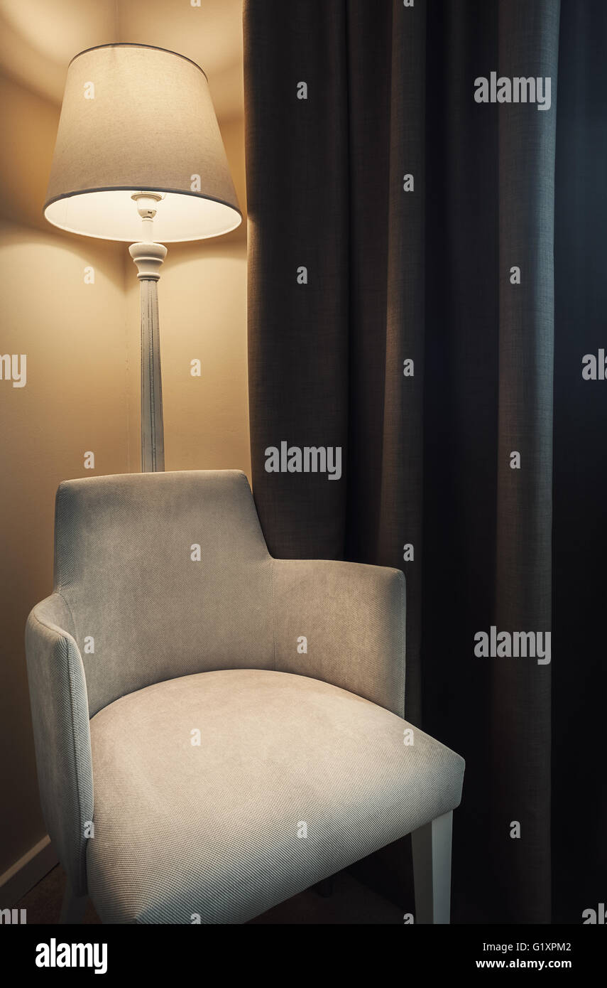 Detalles de la habitación de un hotel, y un sillón, lámparas retro grandes cortinas de color marrón oscuro, ambiente tranquilo durante la noche. Foto de stock