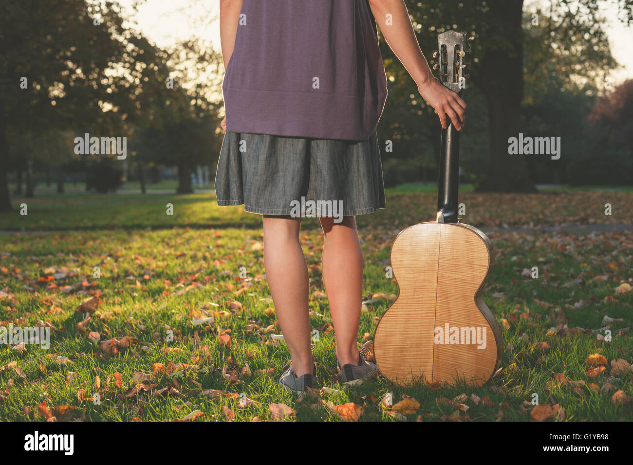 Vista trasera de la foto de un joven con una guitarra permanente en el parque al atardecer Foto de stock