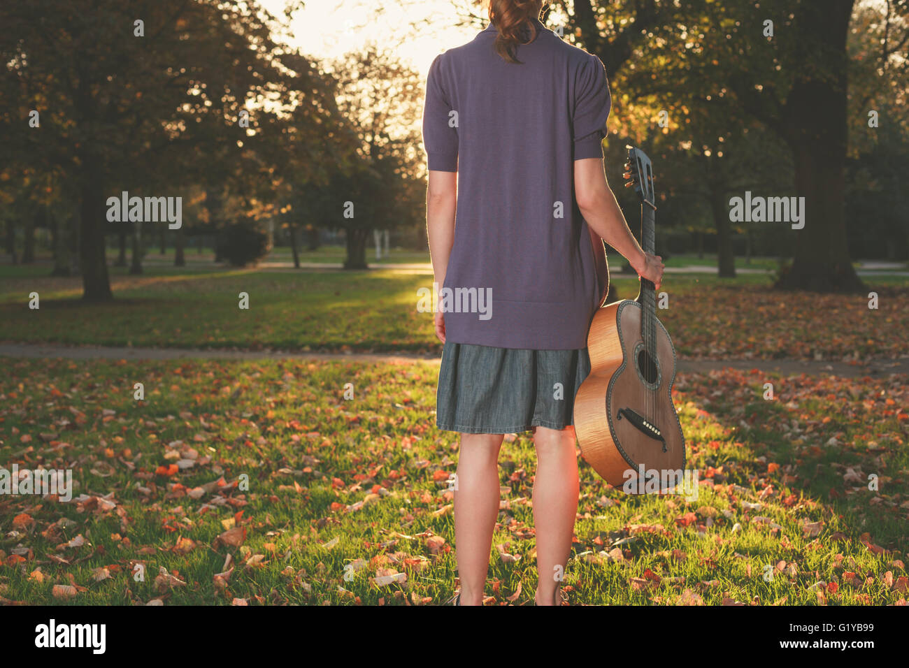 Vista trasera de la foto de un joven con una guitarra permanente en el parque al atardecer Foto de stock