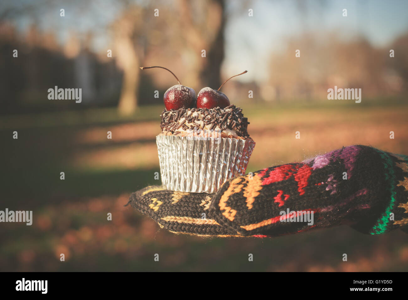 Una mano enguantada sosteniendo una cupcake con una cereza en la parte superior Foto de stock