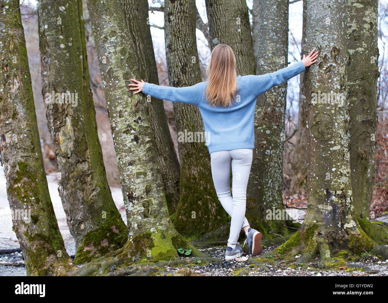 Joven de detrás con largo pelo rubio recostada sobre árboles Foto de stock