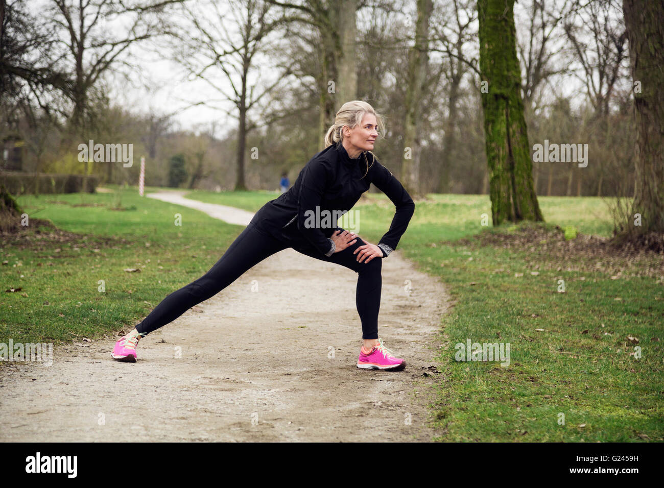 Mujer estirar sus piernas en el parque antes de tener una carrera. Invierno frío día con actividad deportiva Foto de stock