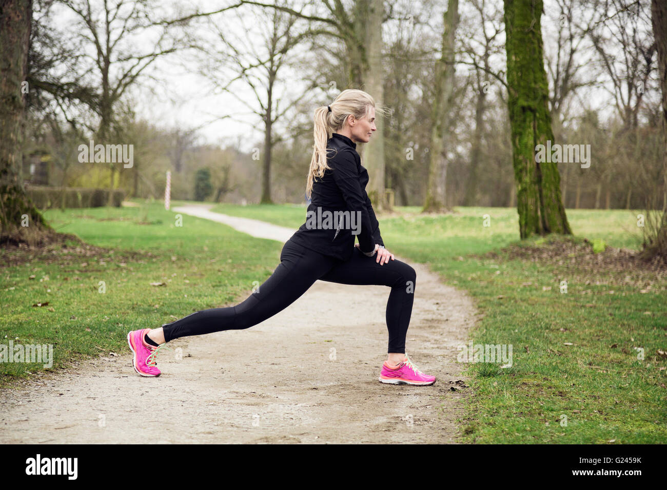 Mujer estirar sus piernas en el parque antes de tener una carrera. Invierno frío día con actividad deportiva Foto de stock