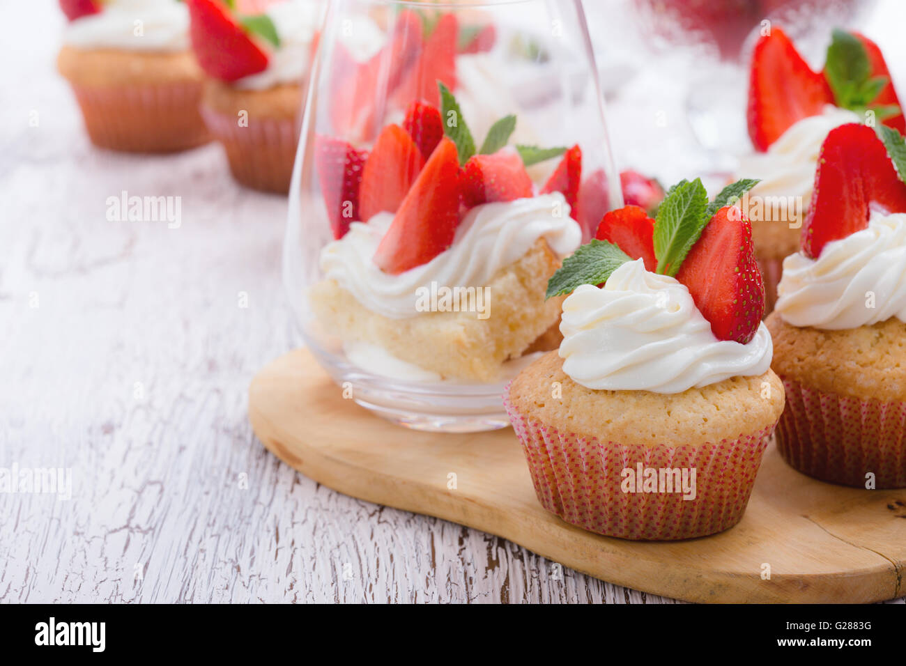 Cupcakes buttercream casero con fresas y menta fresca y esponja layer cake con fresas en un vaso de madera blanca Foto de stock