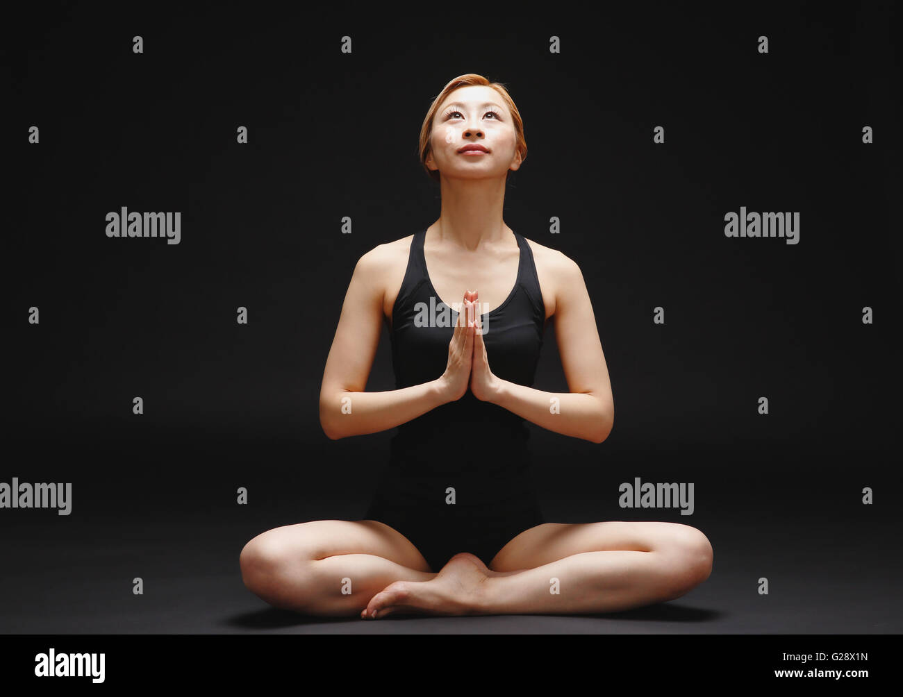 Atractiva jovencita japonesa vistiendo pantalones negros y tank top practicando yoga sobre fondo negro Foto de stock