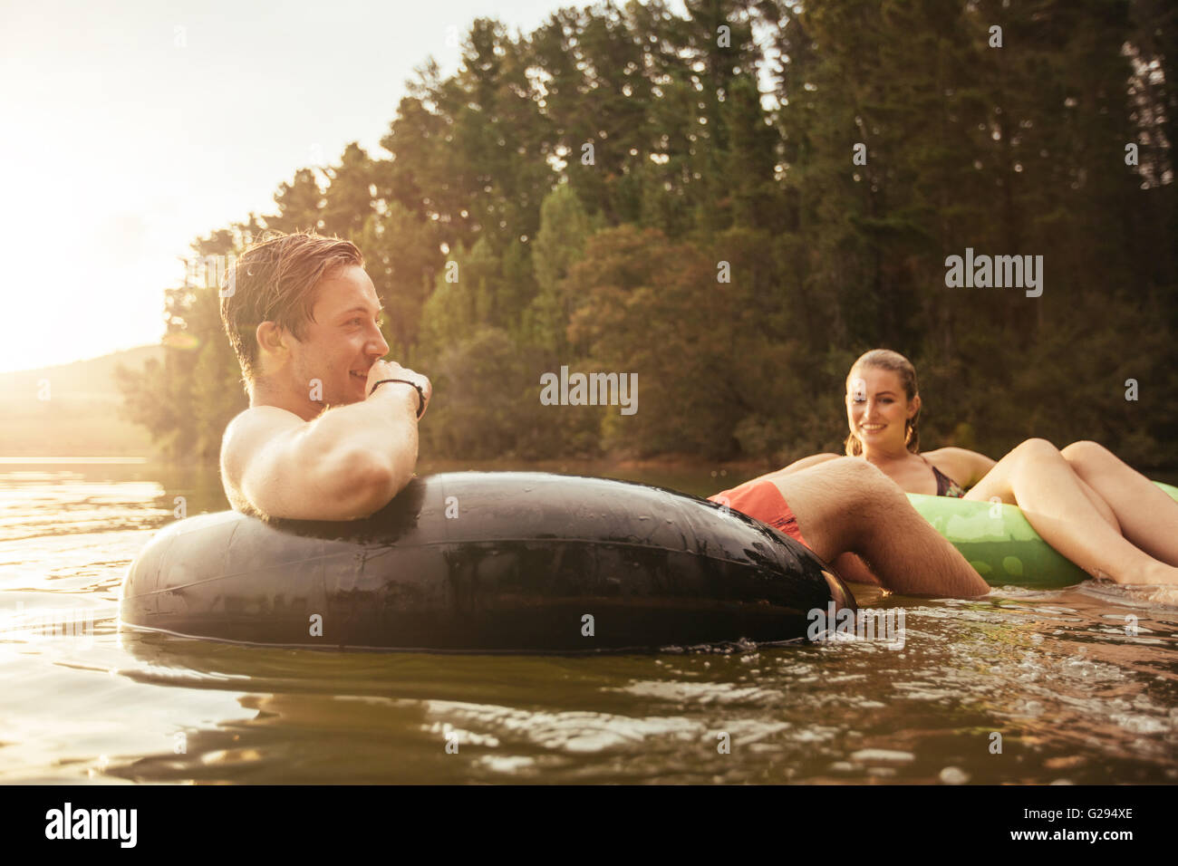Retrato de joven feliz en el lago en el anillo hinchable con su novia. Pareja joven relajándose en el agua en un día de verano. Foto de stock