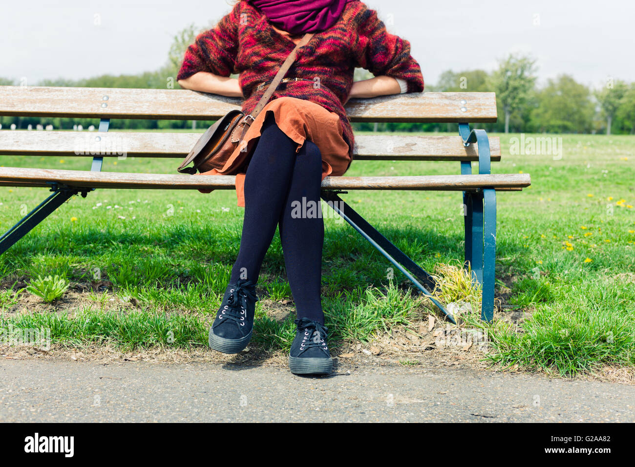 Un joven está sentado y apoyado sobre un banco fuera en un parque Foto de stock
