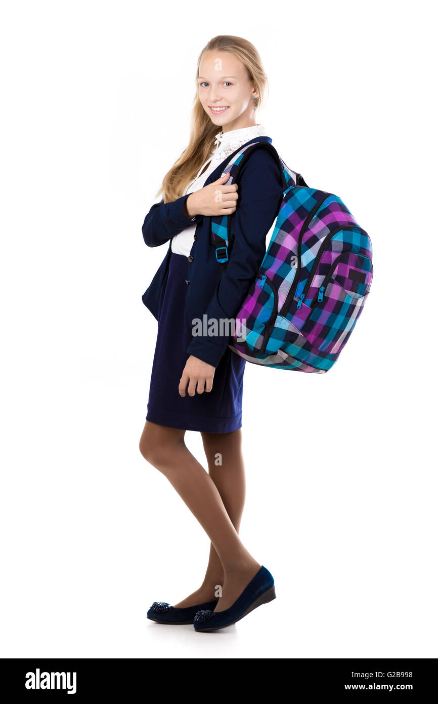 Feliz lindo rubia hermosa colegiala vistiendo uniforme escolar, sosteniendo accidentada mochila con libros de texto, posando Foto de stock