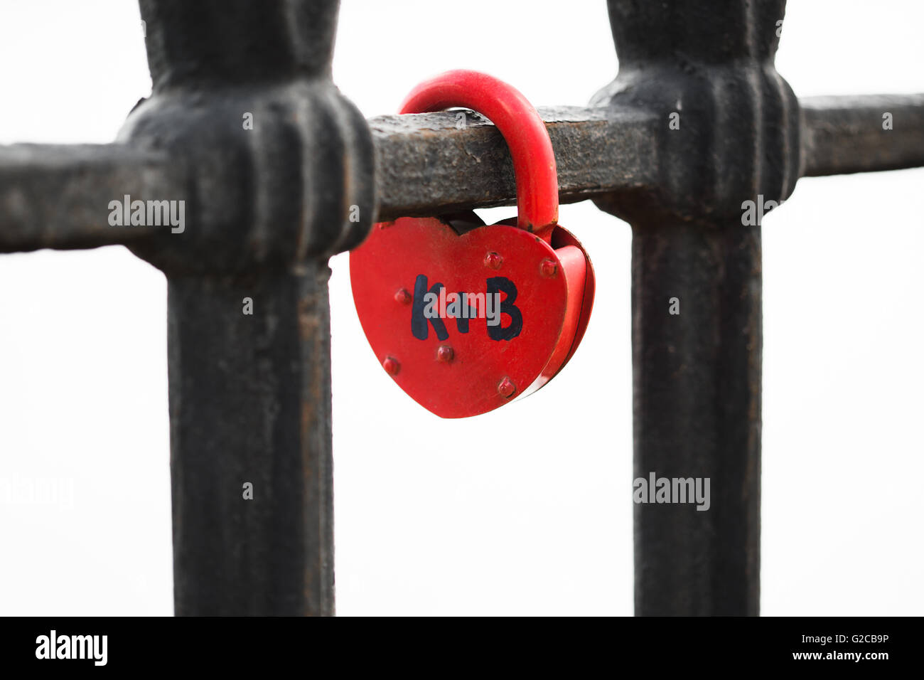 Un candado rojo cerrado en forma de corazón cerrado en el puente. Foto de stock