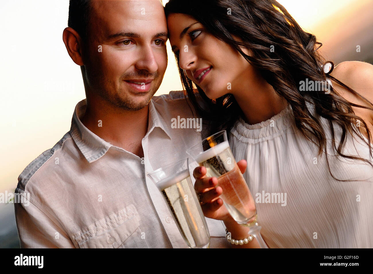 Toast pareja joven vestida de blanco al atardecer closeup Foto de stock