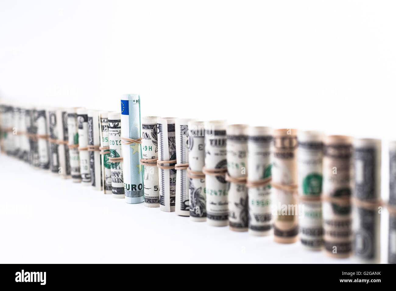 Fila de dollar rollos con un billete de euro en el medio aislado en blanco Foto de stock