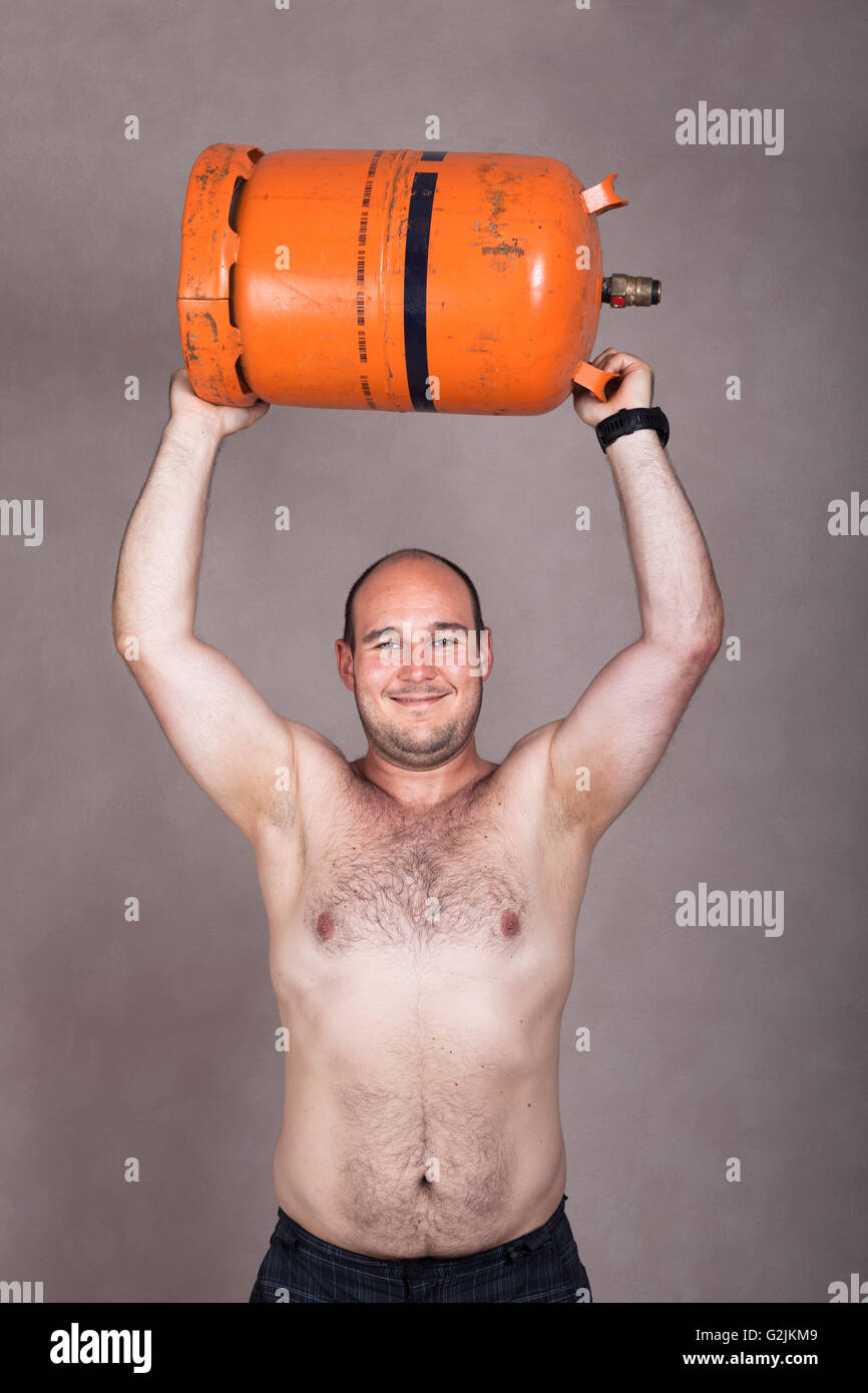 Retrato de feliz fuerte descamisados trabajador hombre levantar pesadas botella de gas. Foto de stock