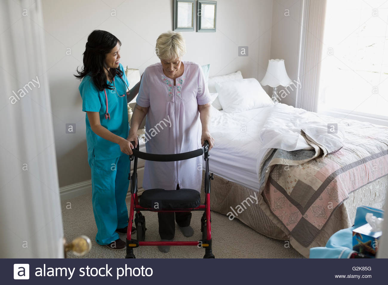 Casa cuidador ayudar a altos mujer con walker en dormitorio Foto de stock