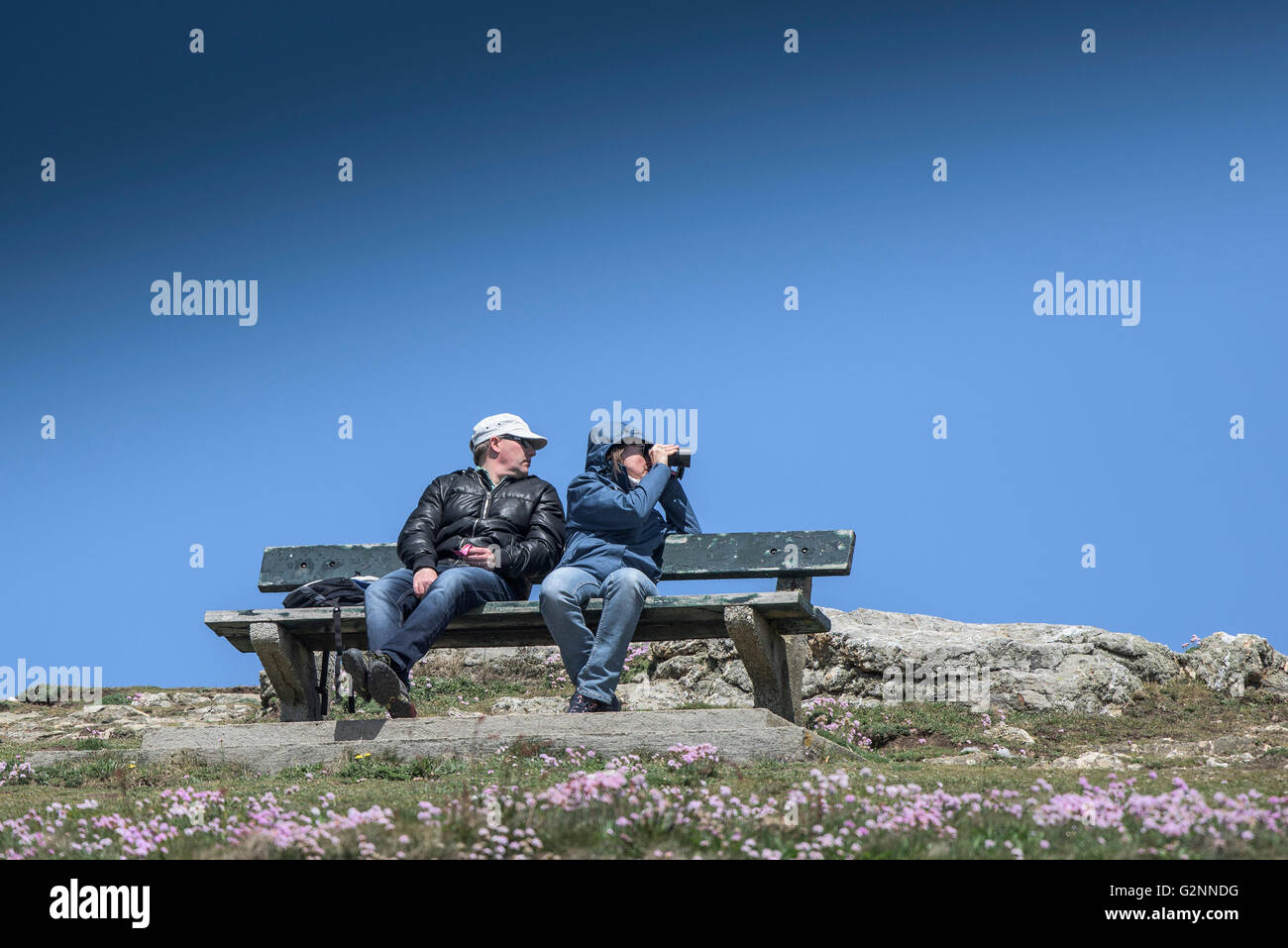 Mucho sol pero con viento como turistas sentarse en un banco en East Pentire cabecero en Newquay, Cornwall. Foto de stock
