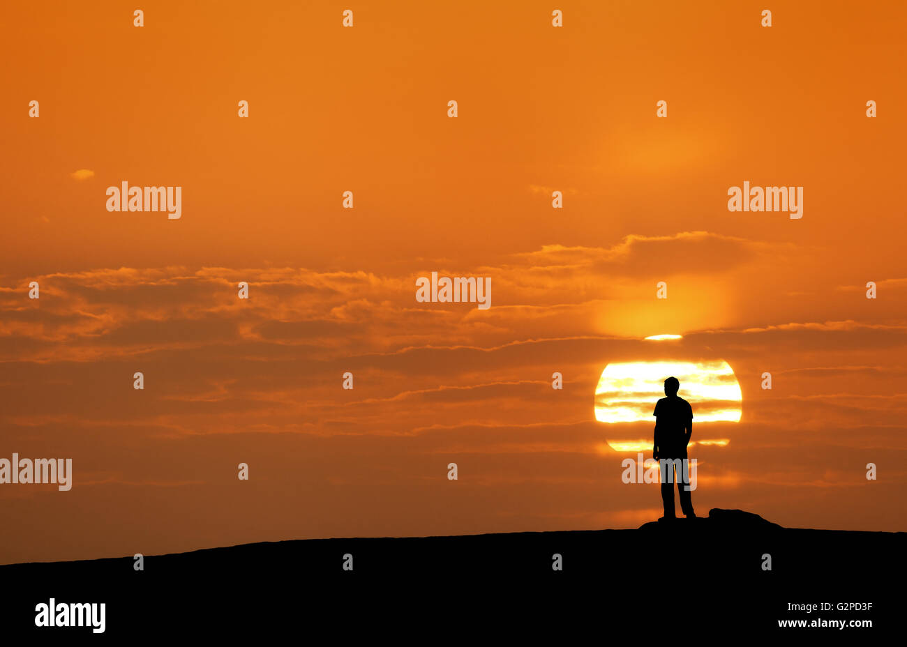 Puesta de sol paisaje con la silueta de un hombre de pie en el fondo del disco solar y coloridos cielo amarillo en verano. Viajar bac Foto de stock