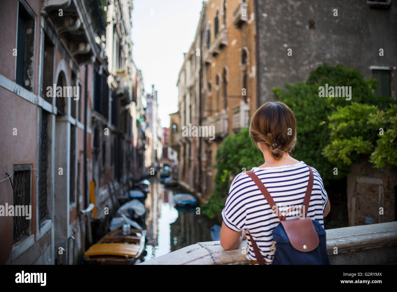 Una mujer joven con una mochila mirando los canales de Venecia tih barcos estacionados al lado de los edificios, Italia. Foto de stock