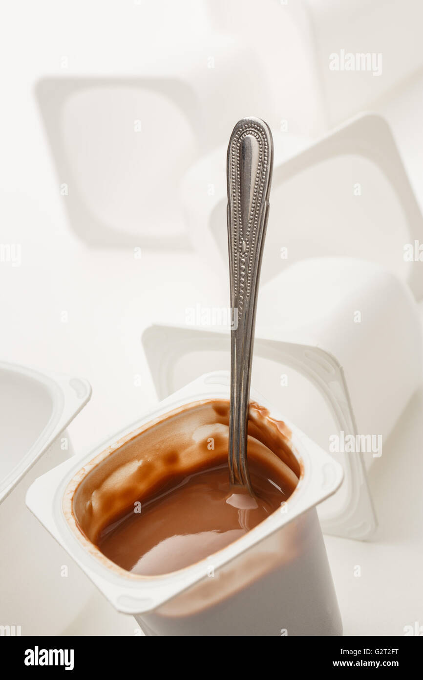 Abra el yogur en la olla con una cuchara de metal y plástico vacío potes de yogur Foto de stock