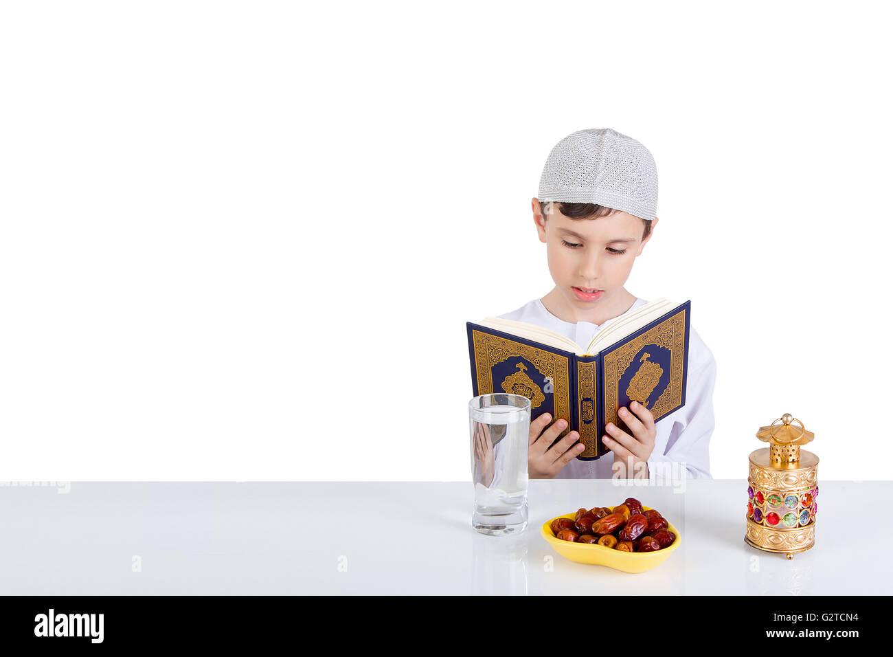 Joven chico leyendo Quraan musulmán en Ramadán - sentado en una mesa con agua , fechas , el Corán, y el Ramadán linterna Foto de stock
