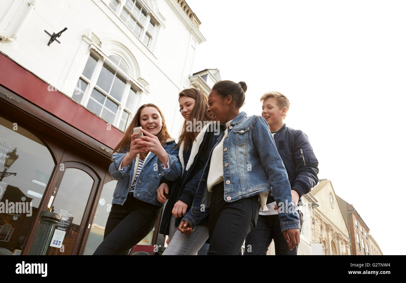 Grupo de adolescentes caminando por la calle mirando los medios sociales Foto de stock