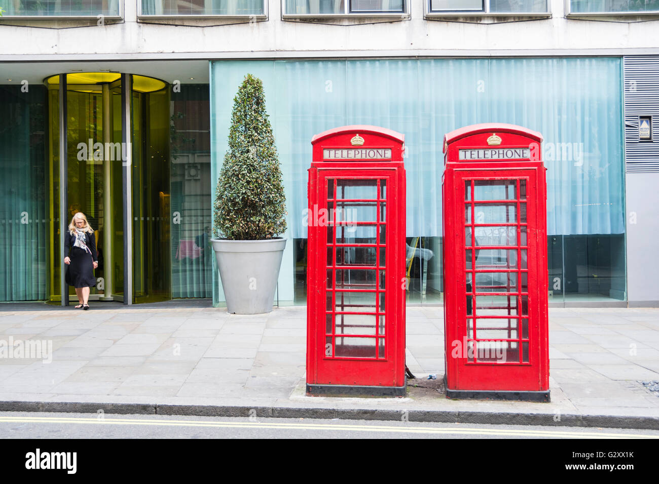Una mujer emerge de una puerta de oficina detrás de dos kioscos telefónicos de Londres Giles Gilbert Scott K6, de grado II, de color rojo brillante, Londres, Reino Unido Foto de stock