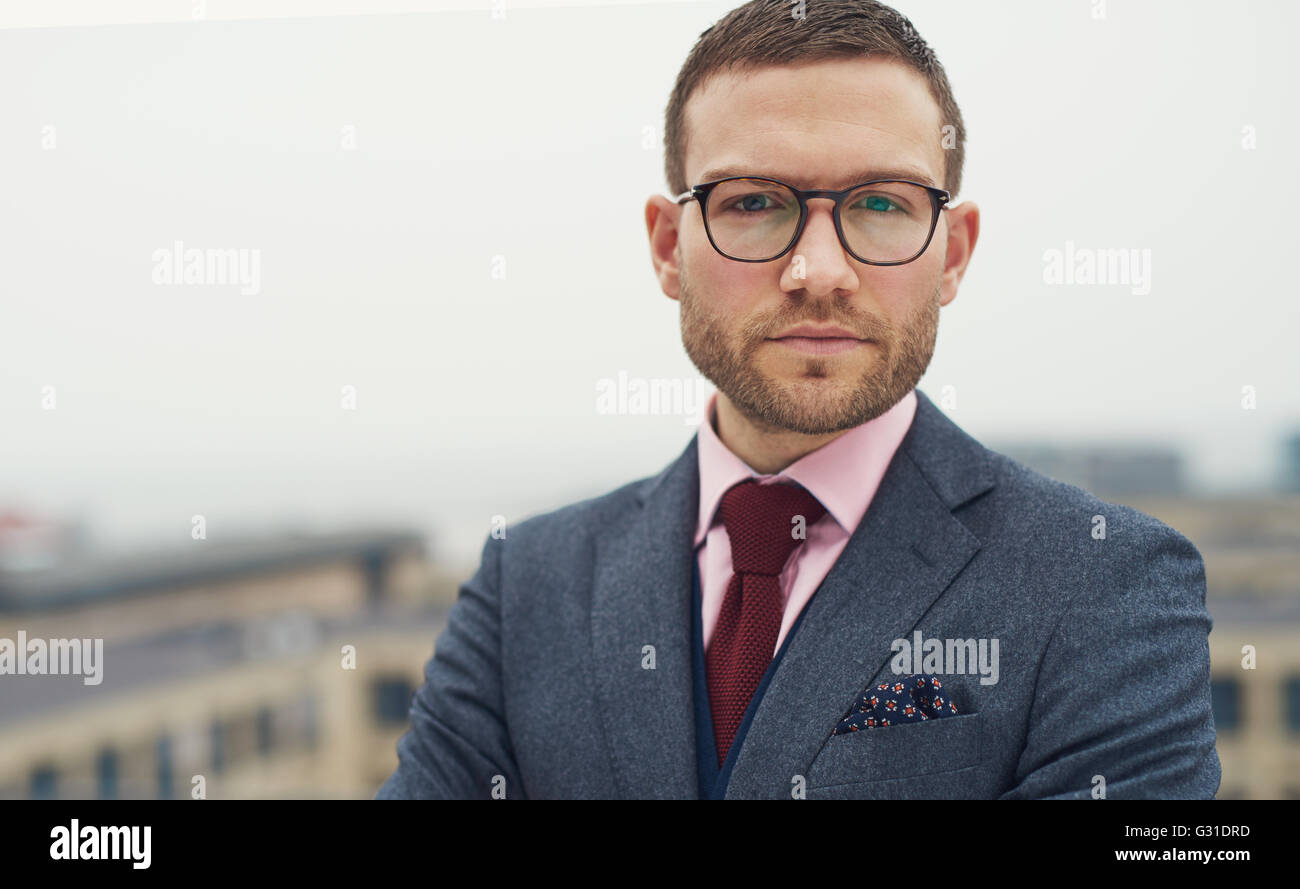 Graves intensos empresario joven con gafas, de pie afuera en un balcón al aire libre mirando a la cámara, la cabeza y el hombro Foto de stock