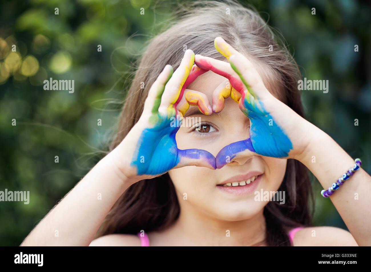 Niña sonriente con manos pintadas haciendo un corazón forma delante de sus ojos Foto de stock