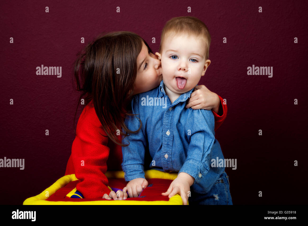 Una niña tira su hermano cercano a besarlo en la mejilla. Él está babeando con su lengua colgando. Foto de stock