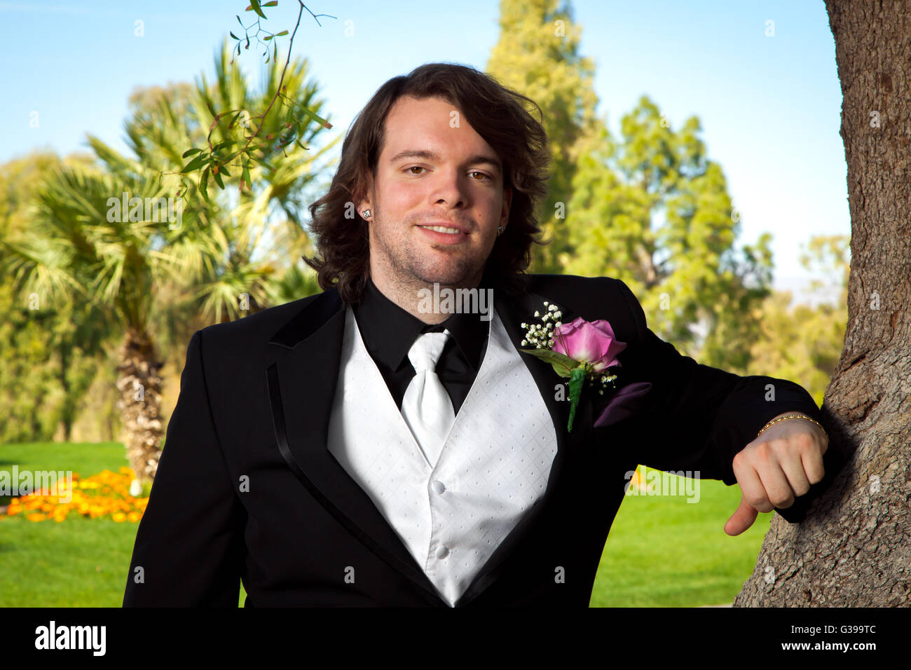 Un novio se inclina sobre un árbol en su día de la boda. Él tiene una rosa rosa arreglo floral para la solapa del novio y un chaleco blanco y corbata. Foto de stock