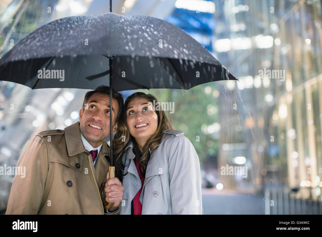 Empresario y empresaria mirando la lluvia bajo el paraguas Foto de stock