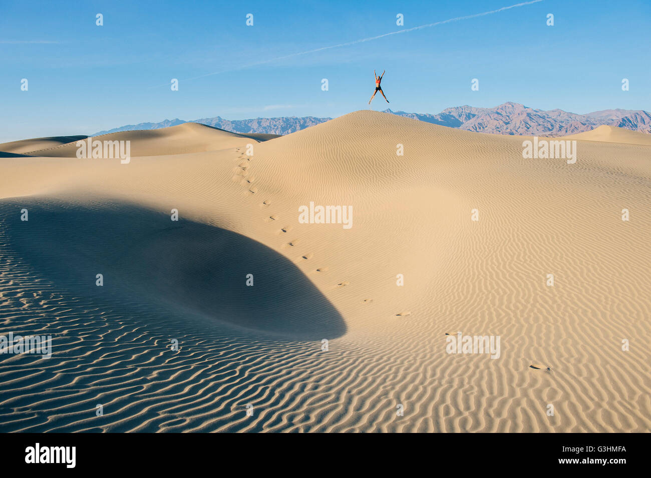 Persona saltando con los brazos y las piernas tendidas sobre una duna de arena, el Valle de la Muerte, California, EE.UU. Foto de stock