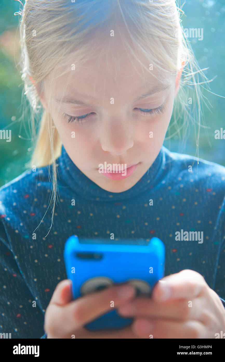 Retrato de niña leyendo textos del smartphone en el jardín Foto de stock