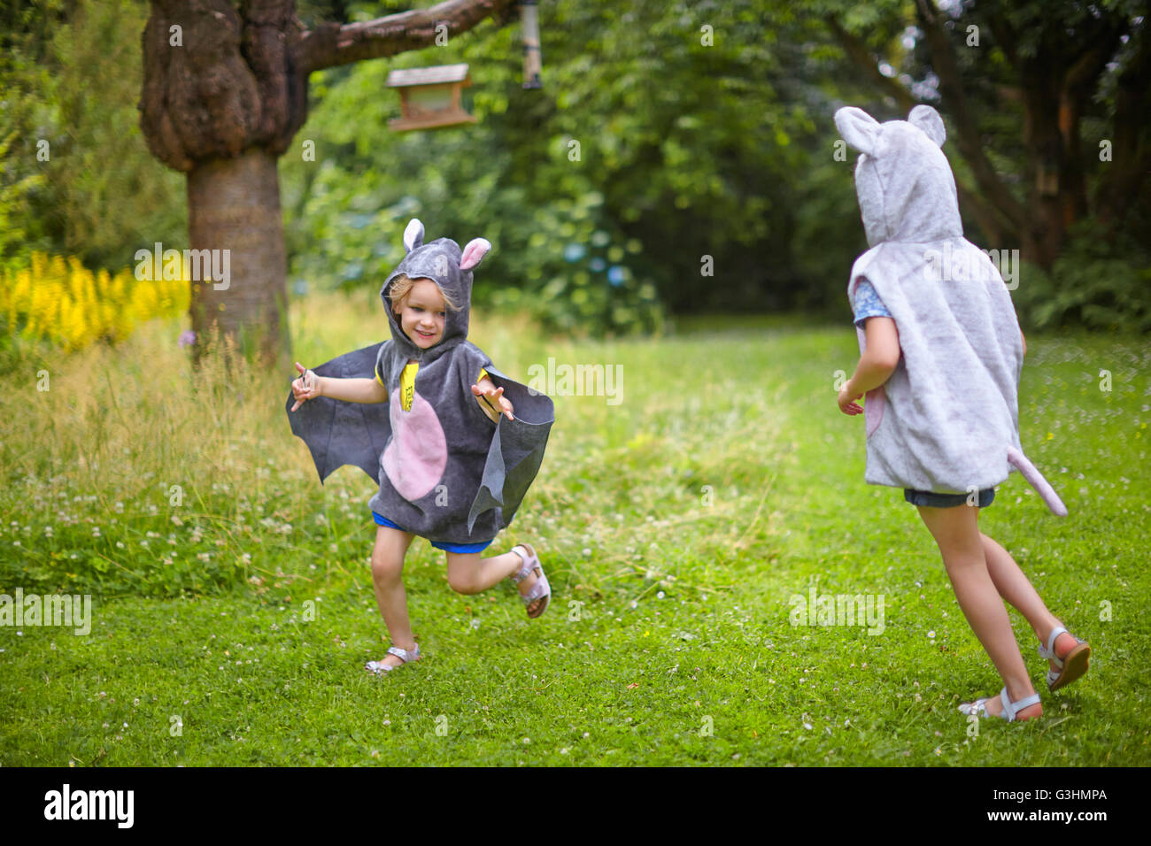 Dos hermanas jóvenes vestidos de traje de ratón corriendo en el jardín Foto de stock