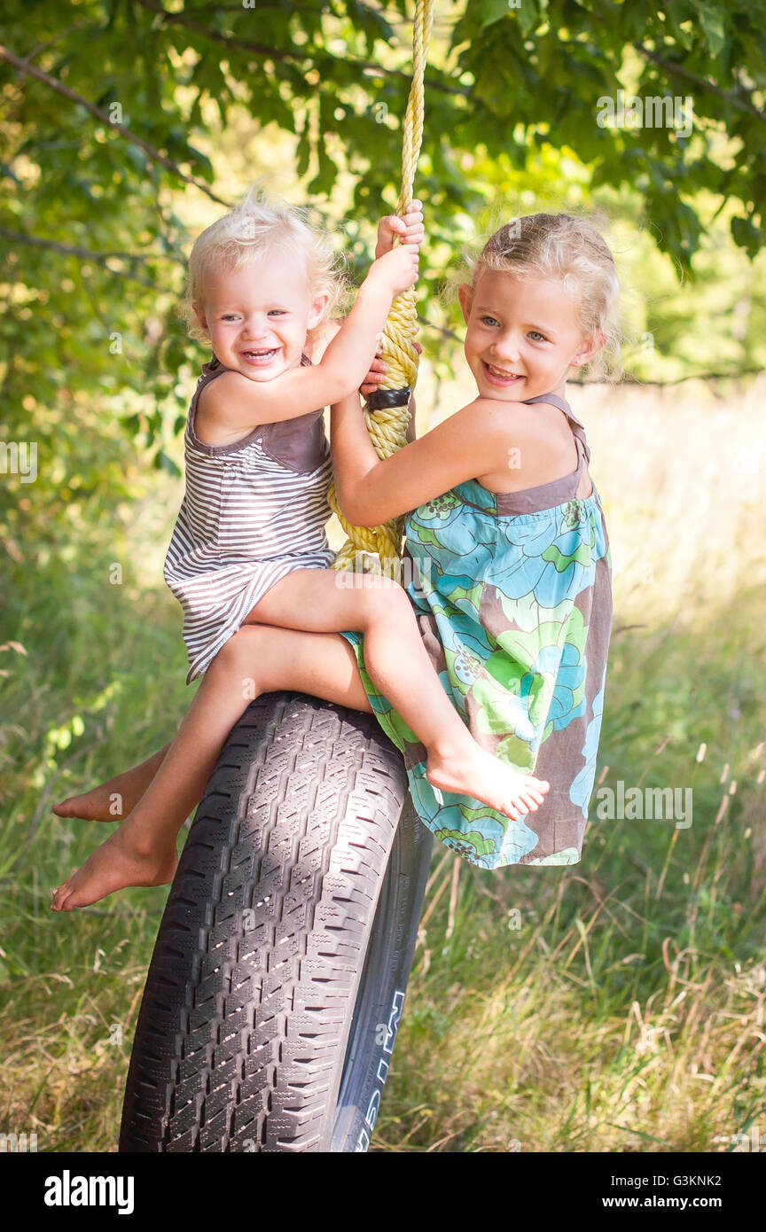 Infante femenino y hermana uno frente al otro jugando en columpio neumático Foto de stock