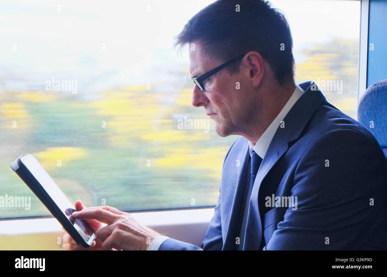 Empresario maduro sentado en el tren, utilizando tablet digital Foto de stock