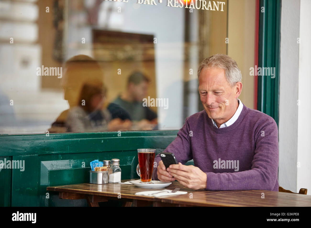 Hombre maduro, lectura de texto smartphone en mesa de café en la acera Foto de stock