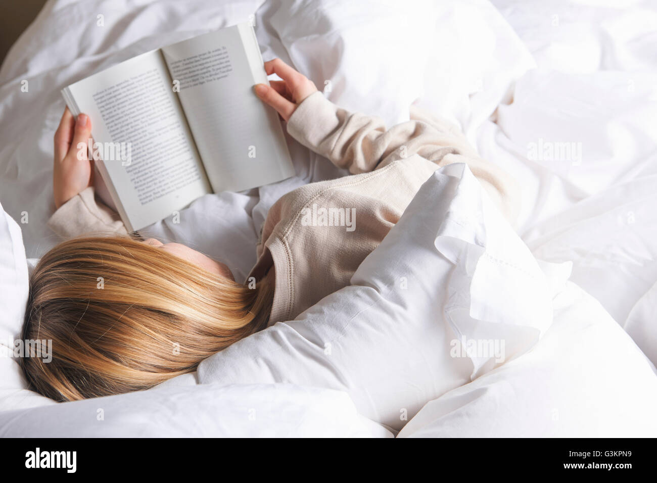 Vista trasera de la muchacha de los cabellos rubios libro de lectura en la cama Foto de stock