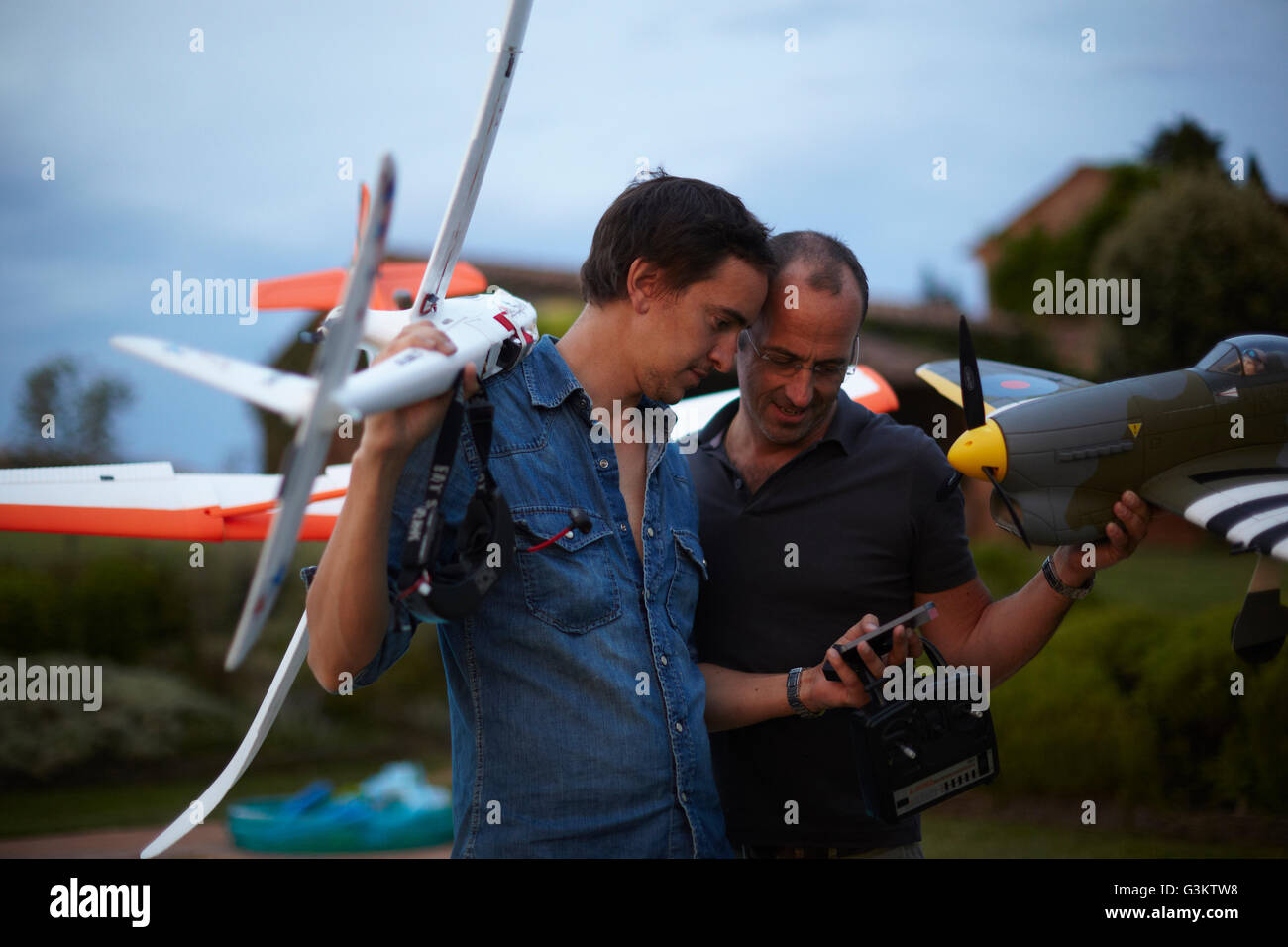 Dos amigos varones mantiene control remoto aviones, mirando el smartphone Foto de stock