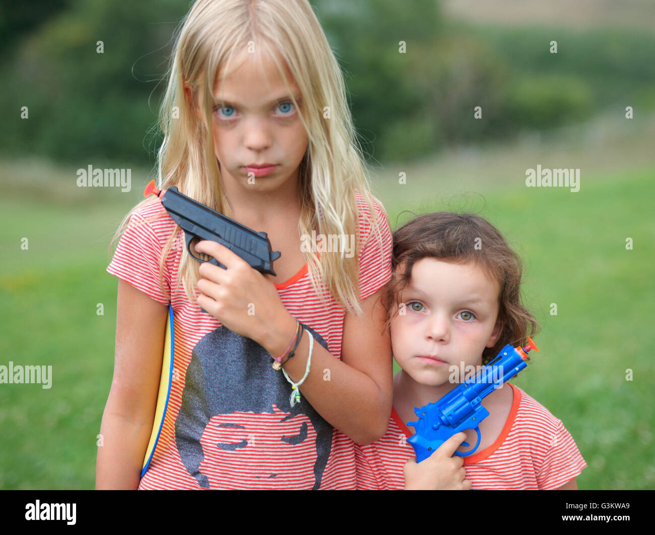 Retrato de dos jóvenes hermanas, sosteniendo pistolas de juguete Foto de stock