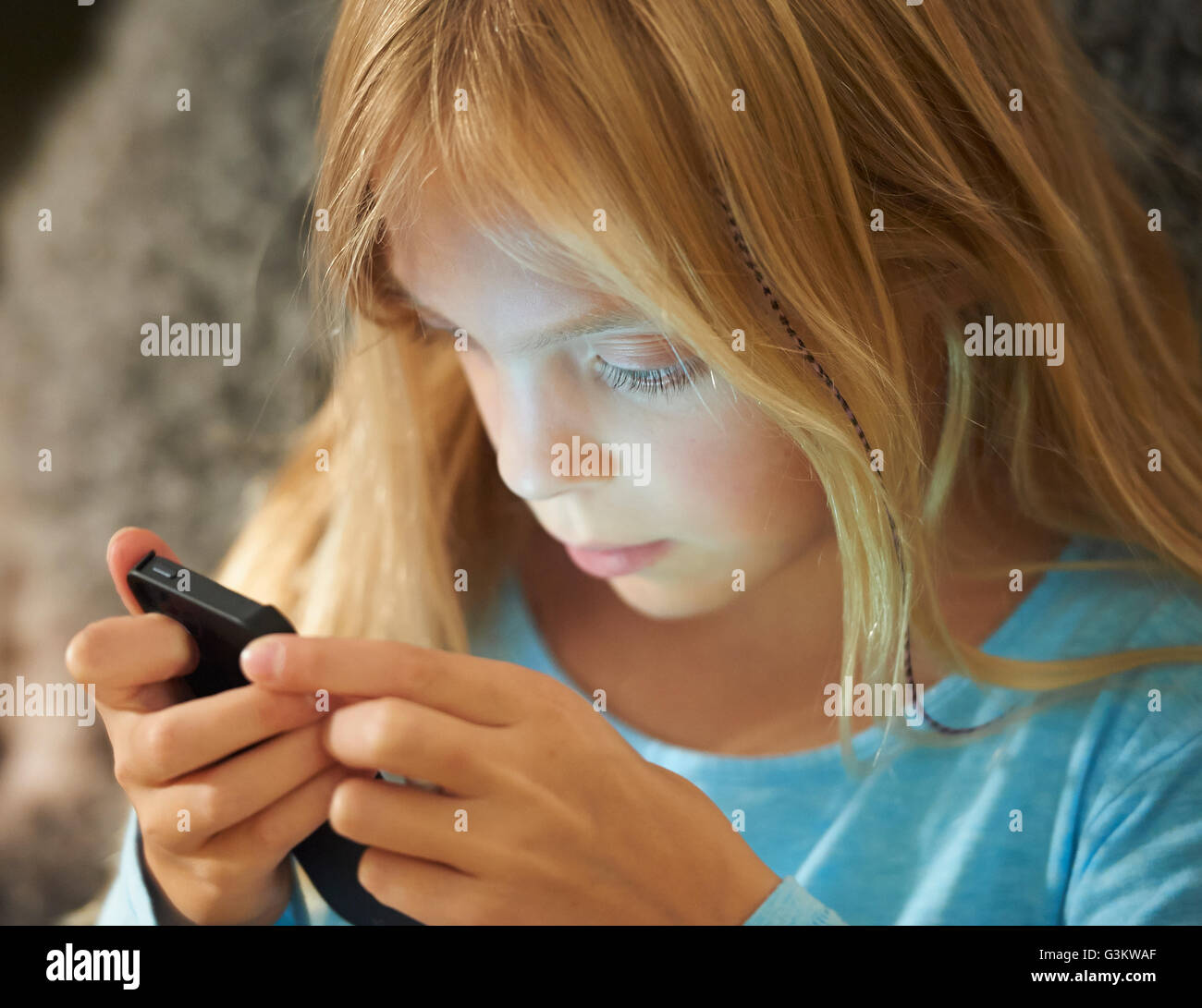 Chica busca en el smartphone, rostro iluminado por el resplandor de la pantalla Foto de stock