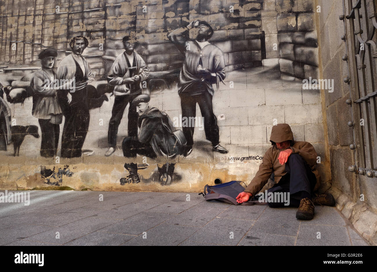 El hombre pidiendo limosna en la calle delante del mural en España Foto de stock