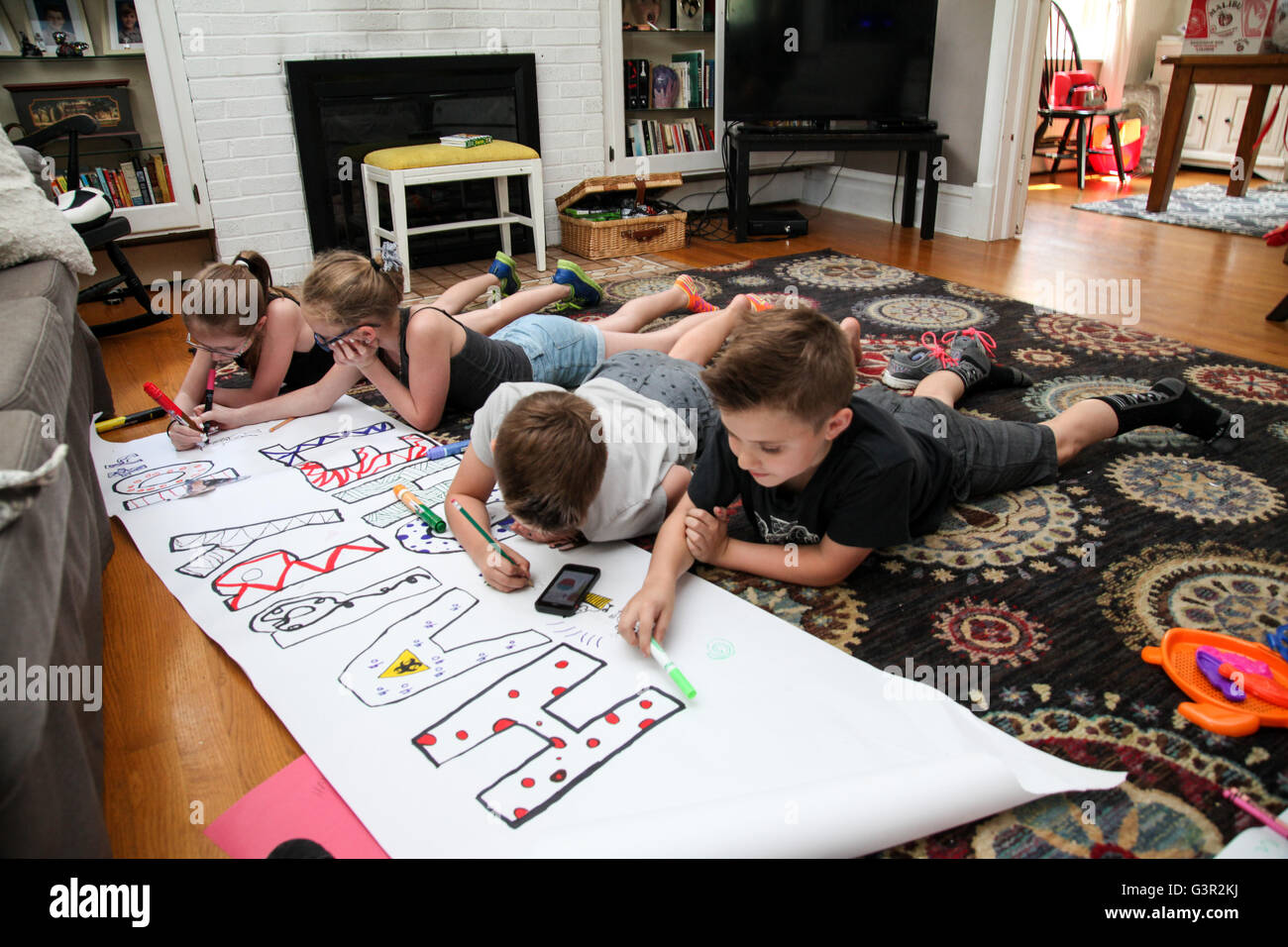 Cuatro niños caucásicos y un bebé sentarse en el suelo y hacer un banner de cumpleaños con marcadores Foto de stock
