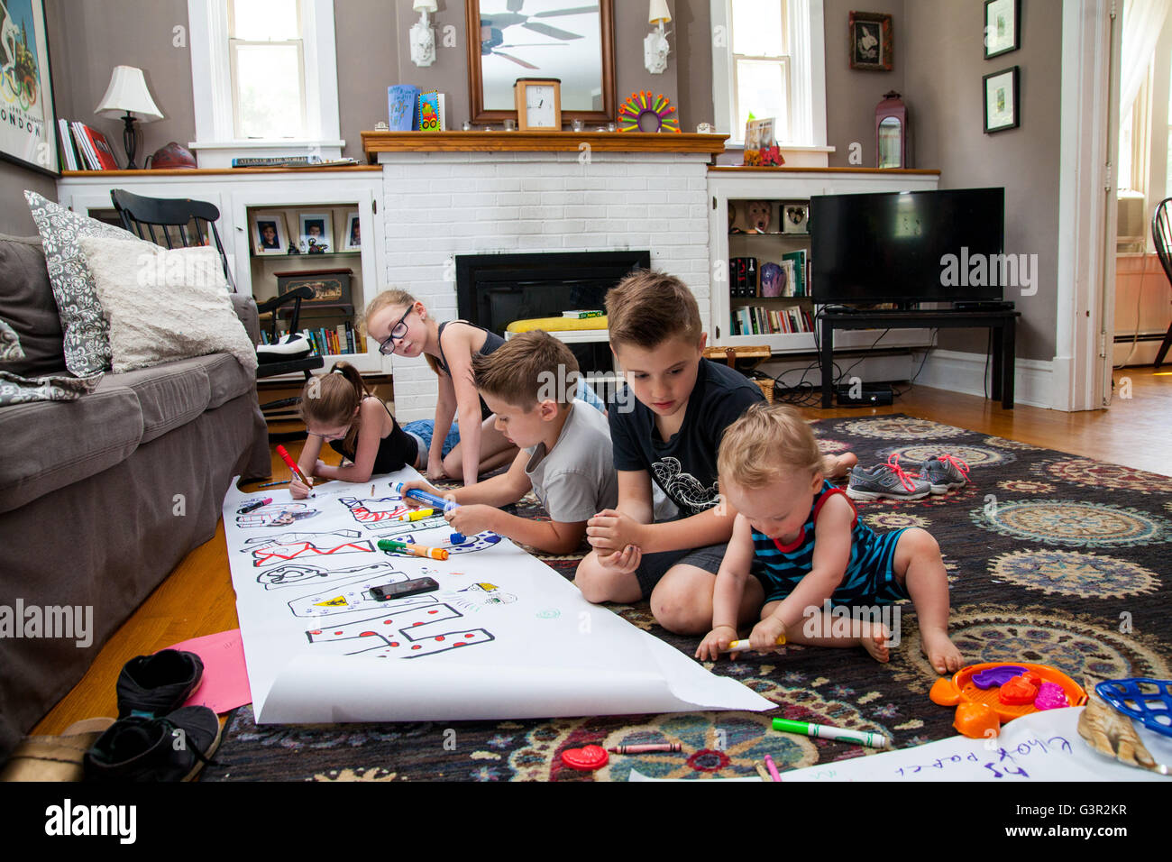 Cuatro niños caucásicos y un bebé sentarse en el suelo y hacer un banner de cumpleaños con marcadores Foto de stock