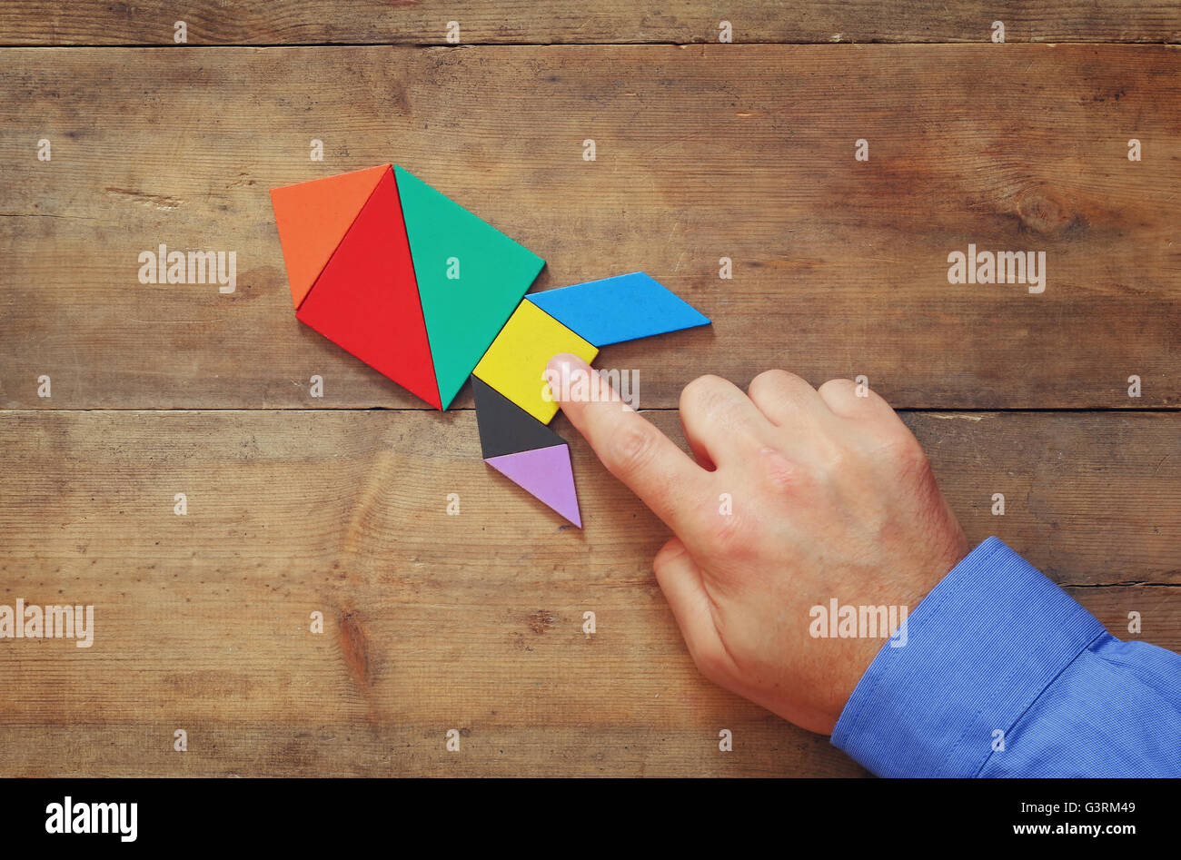 Apuntando a la mano del hombre cohete hecho de cuadrado tangram, fondo de  madera Fotografía de stock - Alamy