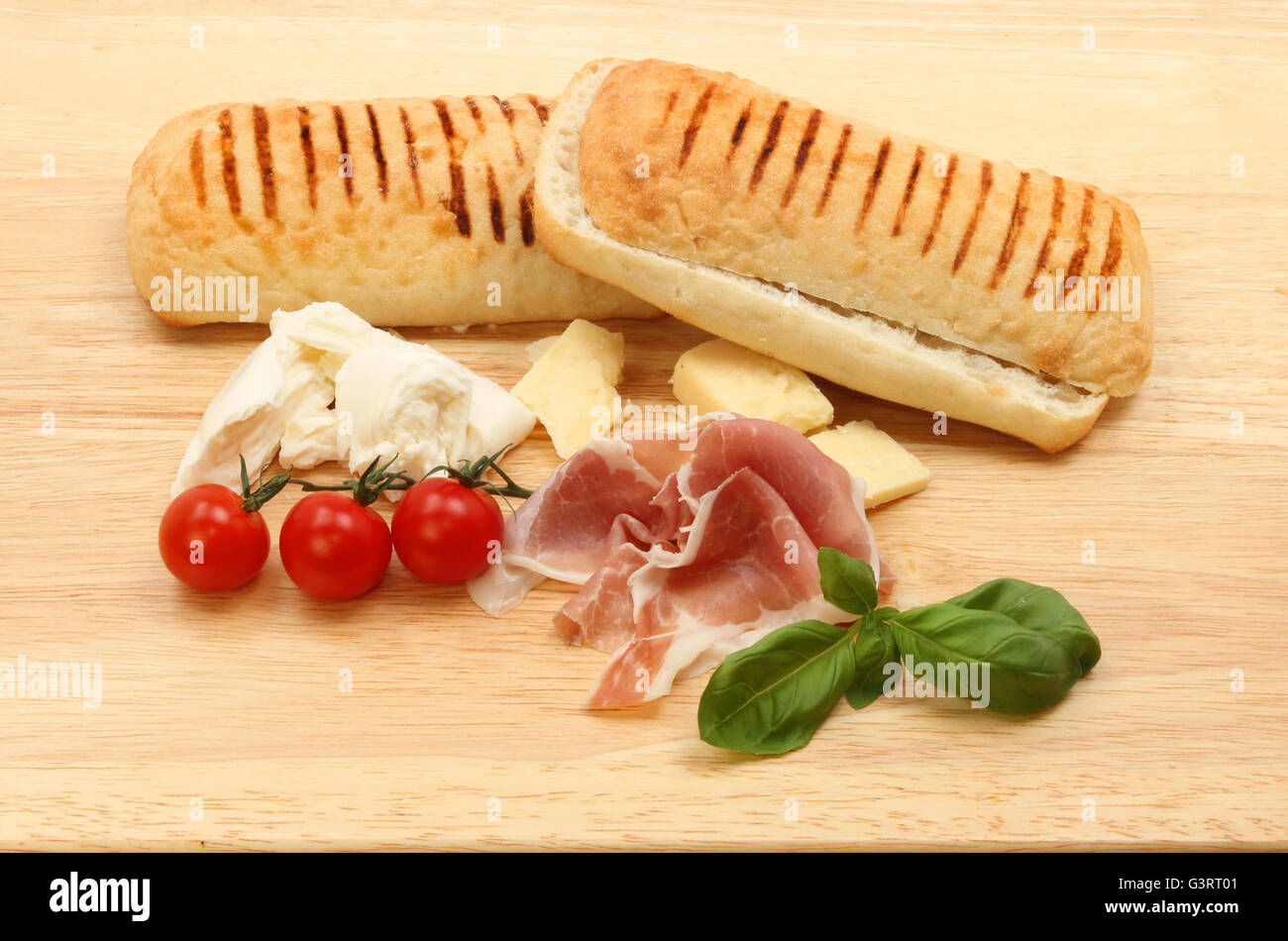 Ingredientes para un jamón de Parma, queso, tomate y albahaca pannini sobre una tabla de cortar de madera Foto de stock