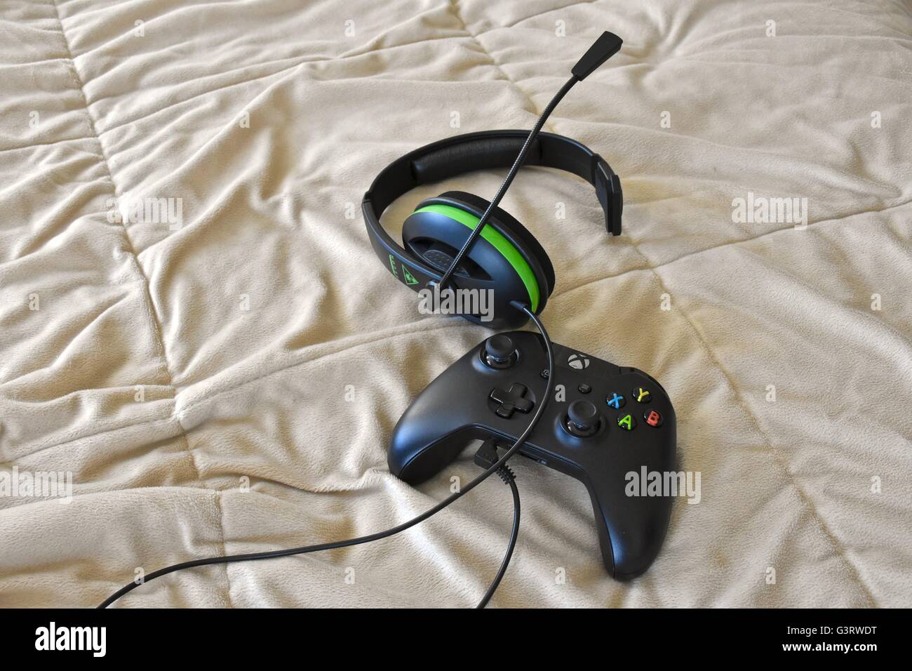 Una Xbox, un controlador y un auricular acostado en una cama Foto de stock