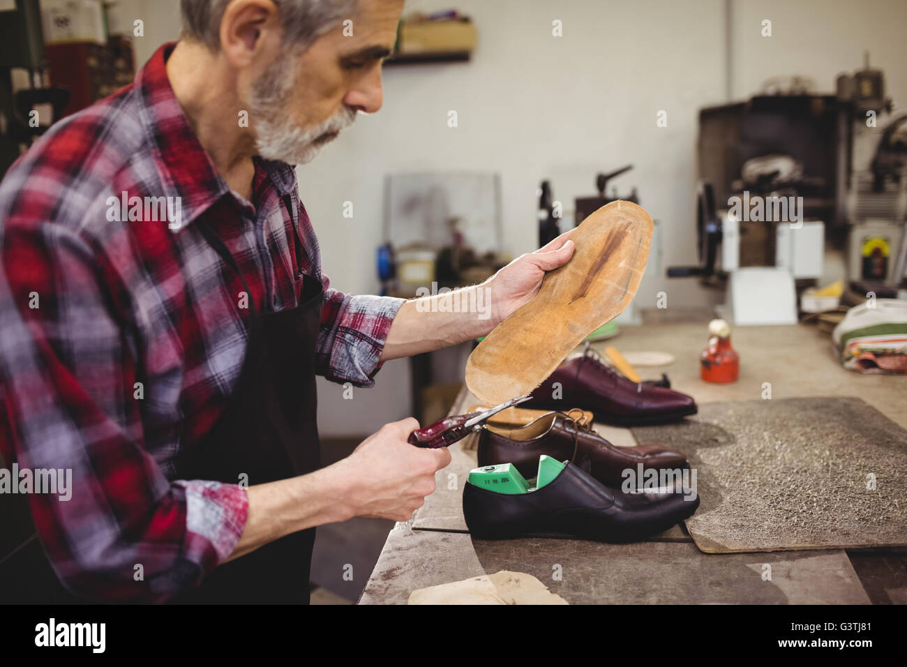 Ver perfil de remendón cortando la suela de un zapato Foto de stock