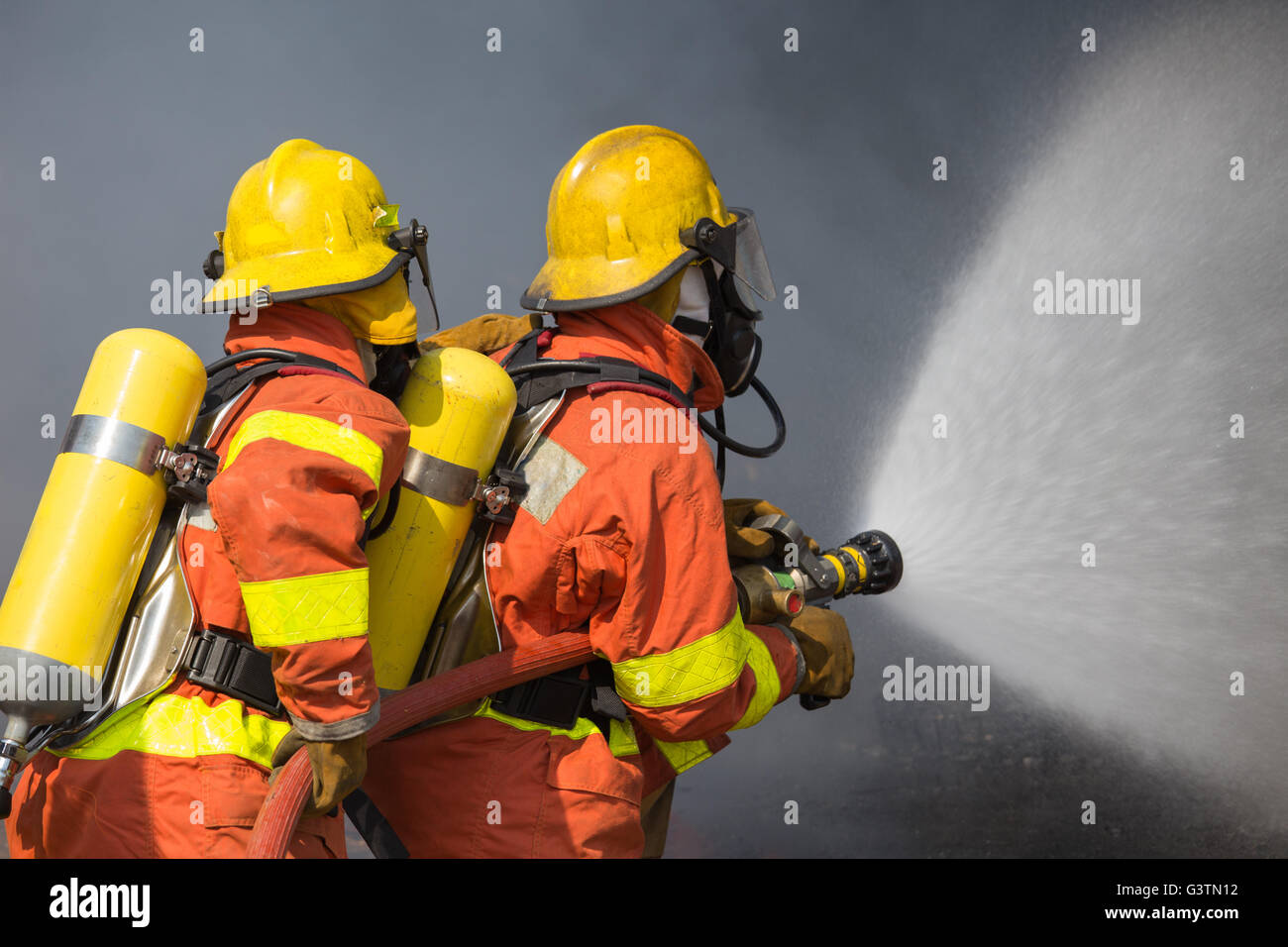 2 bomberos agua pulverizada en la extinción de incendios con fondo oscuro humo Foto de stock