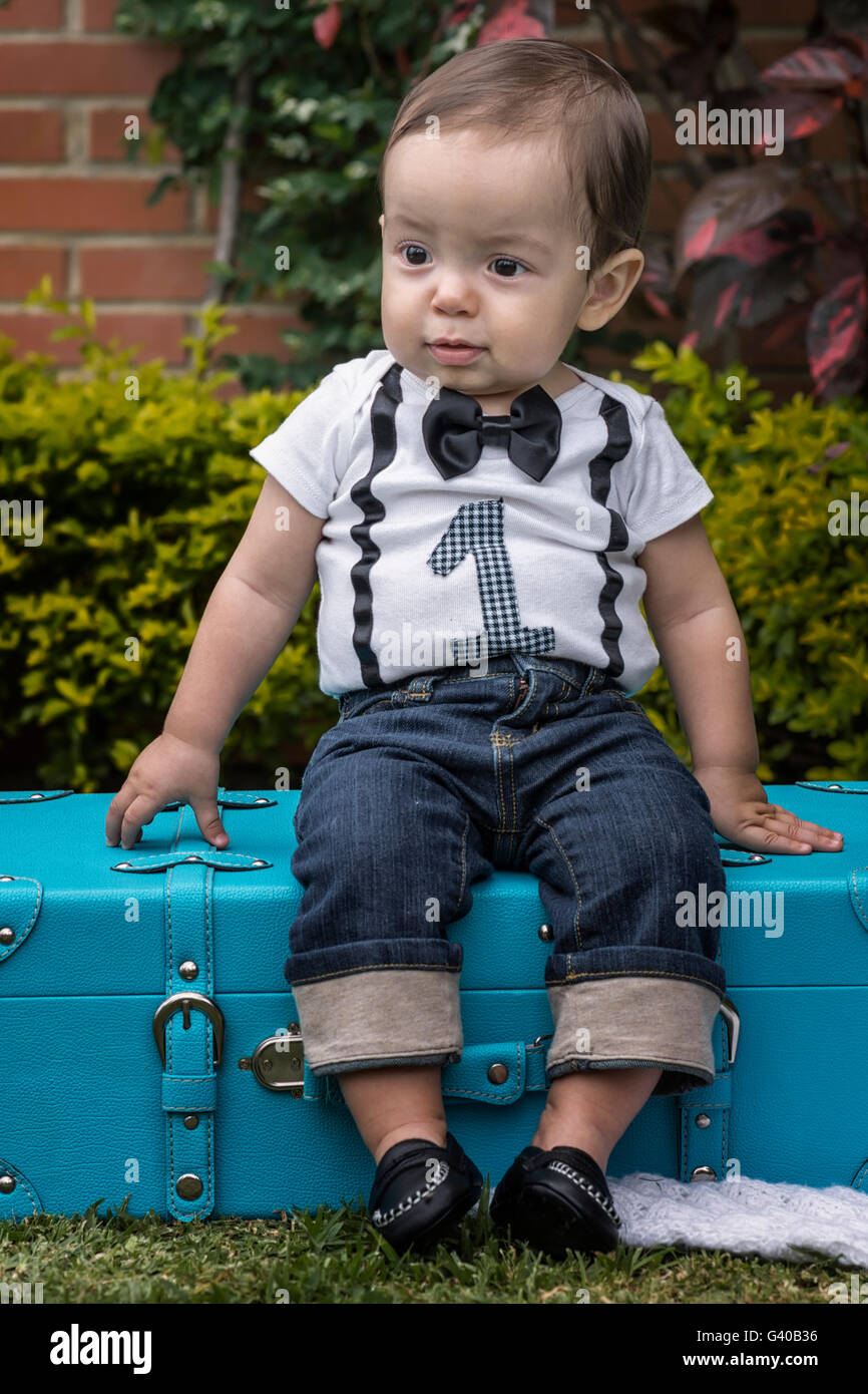 Un año Baby Boy sentado en un equipaje en el jardín Foto de stock